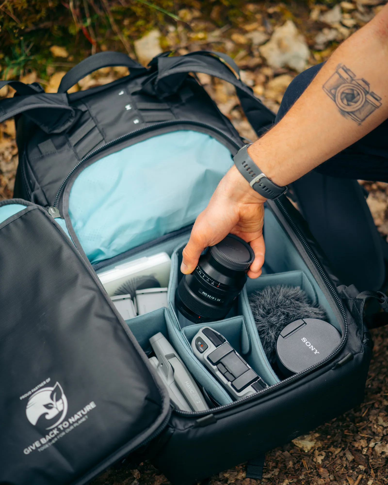Ruka ukládá objektiv do fotobatohu Shimoda v terénu, produktová fotografie pro outdoorové značky