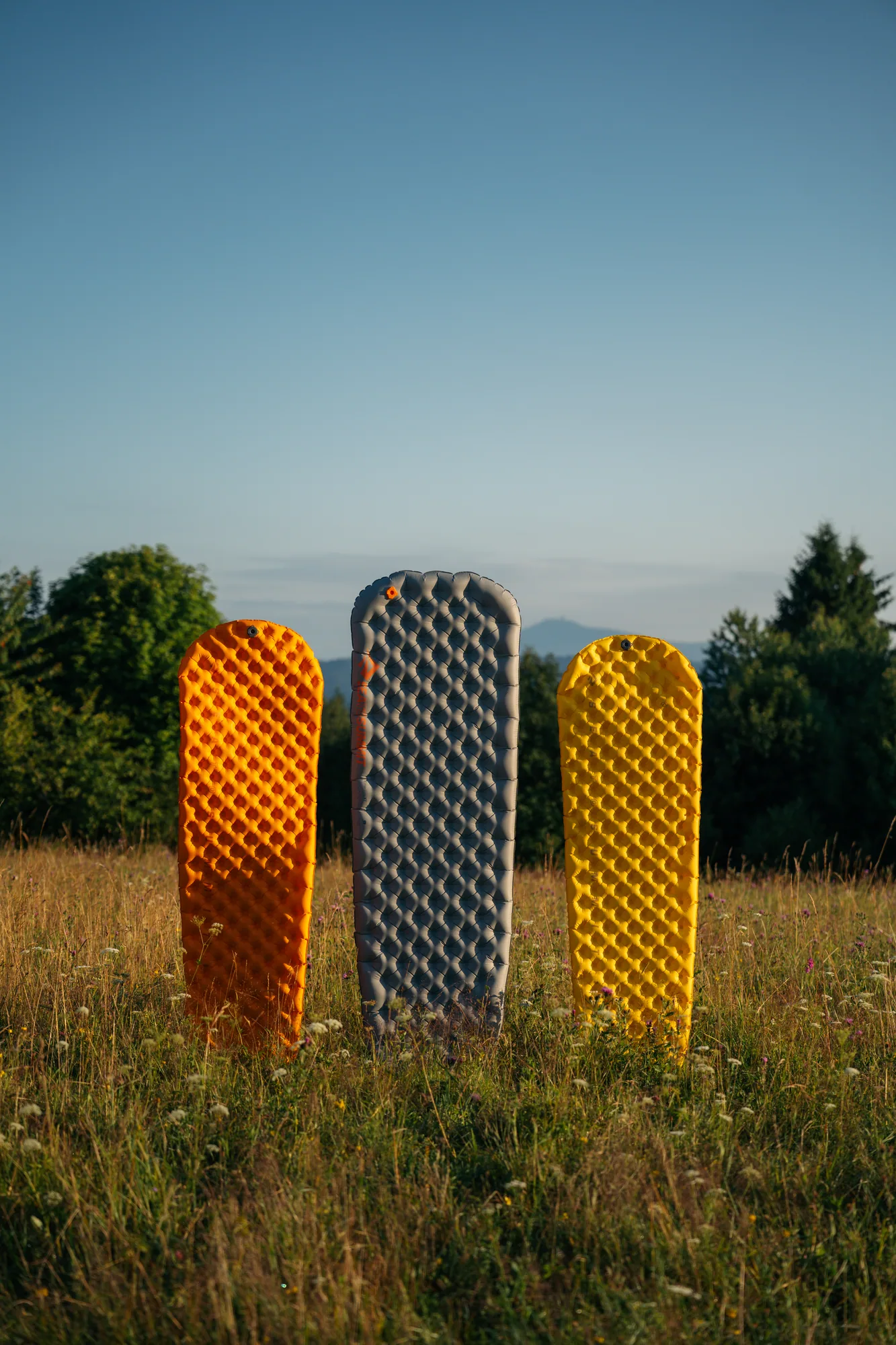 Tři ultralehké karimatky postavené v trávě na horské louce za soumraku, produktová fotografie pro outdoorové značky
